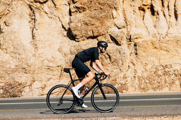 Side view of a young male cyclist riding his bicycle on a road while going up on a hill - obrazy, fototapety, plakaty
