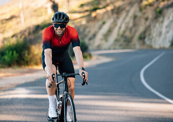 Fototapeta na wymiar Smiling cyclist on a road bike going down a countryside road. Cheerful cyclist in sports attire.