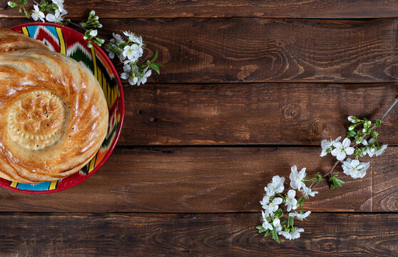 journey cake bread on adras plate decorated with white cherry flowers on wooden background. Navruz, Ramadan postcard
