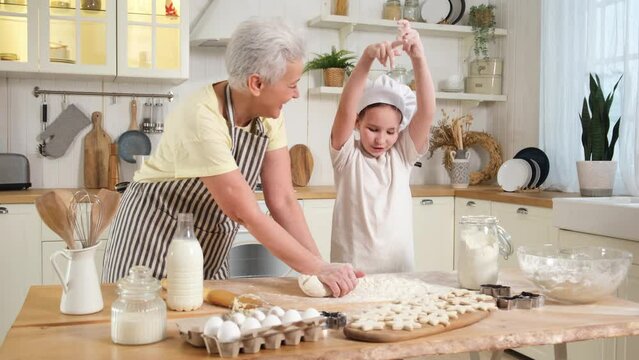 Happy family in kitchen. Grandmother granddaughter child knead dough on kitchen table together. Kid girl playing have fun while grandma cooks bake cookies. Teamwork helping family generations concept