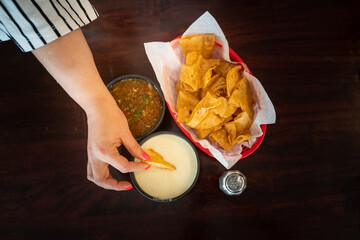 Patron at a mexican restaurant dipping a corn tortilla chip in queso dip