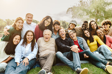 Happy multigenerational people having fun sitting on grass in a public park - 582239379