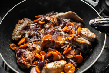 Raw rabbit with spices, onions and carrots in a frying pan. Cooking stewed rabbit.