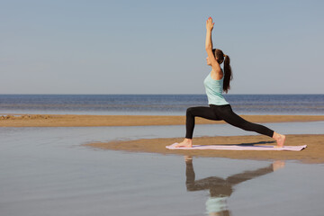 Fototapeta na wymiar yoga, Warrior Pose, sporty woman does warm-up on seashore in morning. fitness millennial female trains, asana breathing practice, healthy lifestyle, love for your body, mental and physical condition