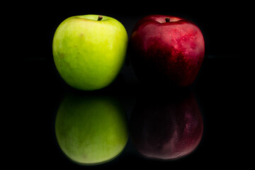a red and a grenn apple on black background with reflection