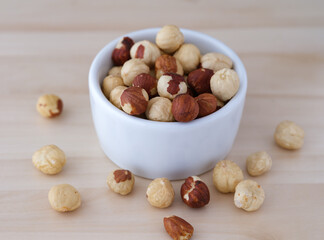 Shelled hazelnuts in a white bowl on wooden background.