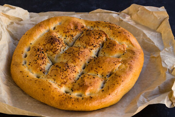 Traditional Turkish Ramadan Bread with oven baking paper on black surface 