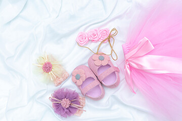 pink baby shoes and flower bow,top view of pacifiers, gifts, hat, booties, bonnets, sneakers, socks, bouquet on pink and blue background