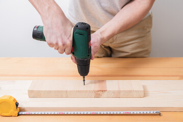 A man works with an electric screwdriver on a wooden table, also makes measurements with a tape...