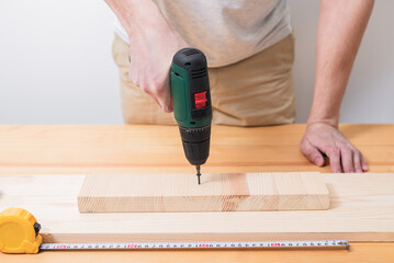 A man works with an electric screwdriver on a wooden table, also makes measurements with a tape...
