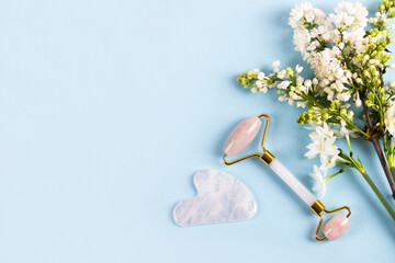 Pink jade roller and gua sha for face massage with flowers daffodils and lilacs. Facial massager tools. Anti age, lifting and toning care. Modern selfcare concept.