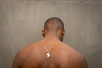 Shirtless handsome young African man with his back to the camera looking down wearing a gold necklace from Africa.