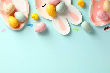 Happy Easter flat lay composition. Frame border made of colorful Easter eggs and bunny and egg shaped plates on pastel blue background.