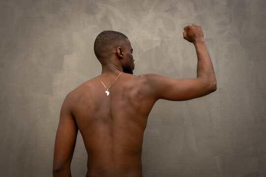 Shirtless muscular african young man on grey background with necklace african pendant with fist up
