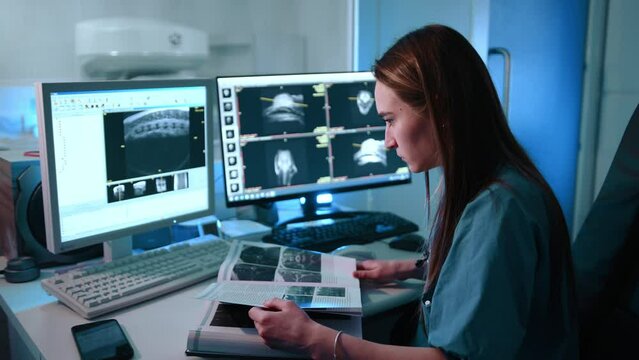 A veterinarian looking for simularities with magnetic resonance images on their computer and in the book. They look focused on their work. High quality 4k footage