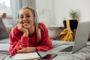 A college student is laying on the bed with laptop in front of her
