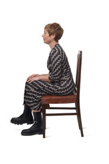  side view portrait of a woman in dress and boots sitting on chair with croos legged on white background