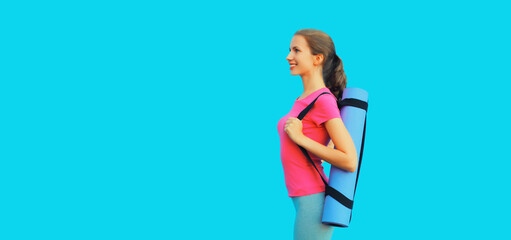 Sport and fitness concept - portrait of happy smiling young woman in sportswear with yoga mat on blue background