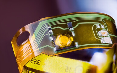 Closeup of electronic flexible printed circuit on plastic strip curled to ring on purple background. Green and yellow lines and small electric components on flex PCB strip from disassembled earphones. - obrazy, fototapety, plakaty