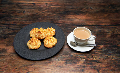 cookies made from coconut, egg, sugar and flour on a black rock plate next to a cup of latte