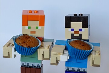 Fototapeta premium LEGO Minecraft larger figures of Steve and Alex, both holding small, bronze baked muffin cupcake in a blue paper cup. 