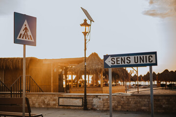 One-way signs and pedestrian crossing on the access road to the beach, in the sunrise light. Straw...
