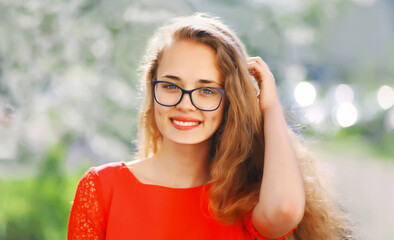 Portrait of happy caucasian smiling young woman in eyeglasses in spring garden park on flowers background