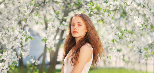 Naklejka na ściany i meble Portrait of beautiful cute young woman with long curly hair in spring blooming garden on white flowers background