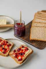 Bread with butter and cranberry jam is on the table and ready to eat. A delicious and sweet breakfast. Aesthetically pleasing serving of food. Recipe for toast with butter and jam.