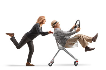 Woman pushing an elderly man inside a shopping cart holding a steering wheel