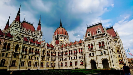 Fototapeta na wymiar Orszaghaz, Budapest, Hungary - June 5, 2018: exterior of the side of the Hungarian Parliament Building under a cloudy sky with the Hungarian flag