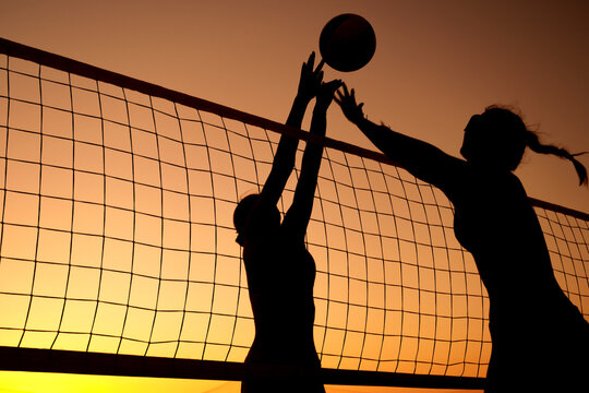 Silhouette women playing beach volleyball on sunset. - Powered by Adobe