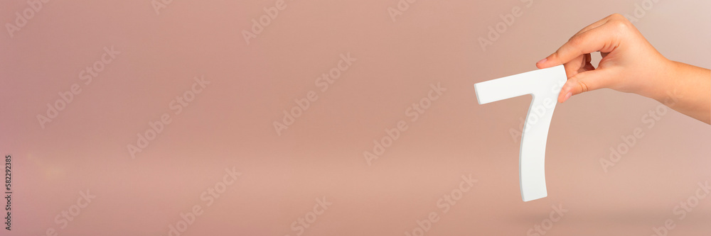 Aufkleber number seven in hand. hand holding white number 7 on red background with copy space. concept with nu
