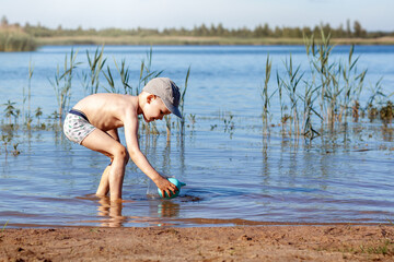 Summer time and rest near the water. Little joyful Caucasian funny boy plays and enjoys in the lake. The child is resting and playing in the lake pond sandy beach