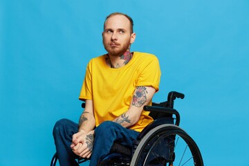 a man sits in a wheelchair in a t-shirt on a blue background in the studio, the concept of a free barrier-free environment for people with disabilities