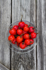 ripe red rosehip berries in a glass bowl on wooden table