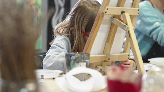 a little girl paints a painting on canvas in an art studio.