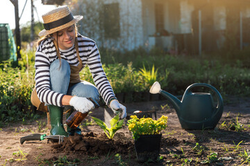 Stylish young woman-gardener replant plants from a pot in the garden