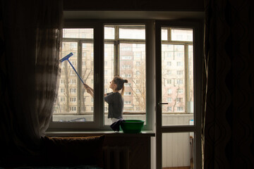 The girl washes the window in the apartment, cleaning the house