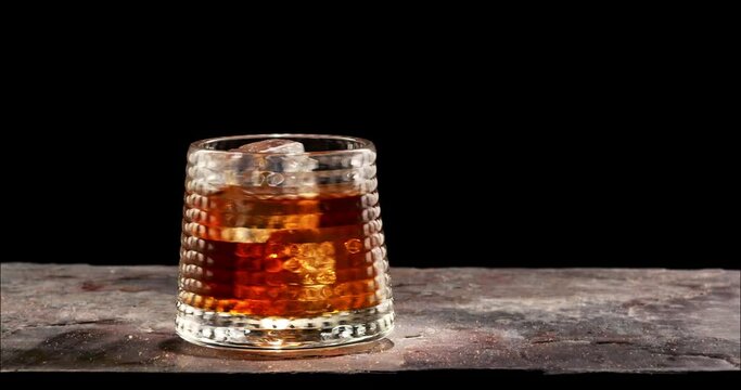 Glass of whiskey with icecube spinning on table. Slow motion, copy space, black background. Whiskey, brandy, cognac, alcoholic drink .
