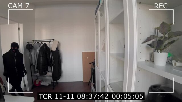Surveillance camera of a burglar in a mask robbing a house. CCTV television recording.