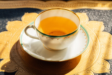 dainty white teacup with green and gold border on gold and black tray in the afternoon sun