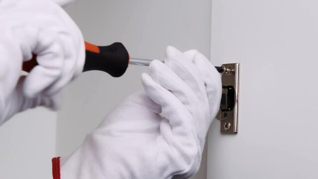 a man in white gloves screwing a furniture door hinge with a screwdriver