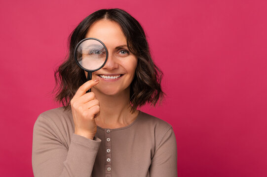 Good looking smiling mid age woman is looking through a magnifying glass.