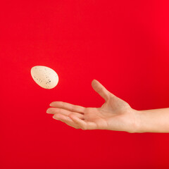 Woman's hand throwing away white egg on red background. Minimal Easter concept. Copy space.