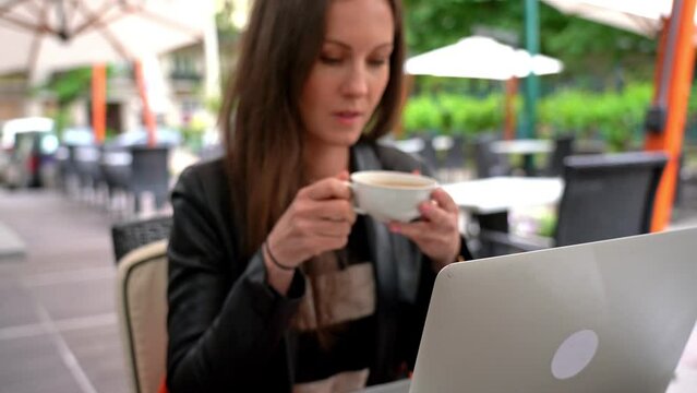 Young adult woman drinking tea and working with laptop computer on restaurant terrace.