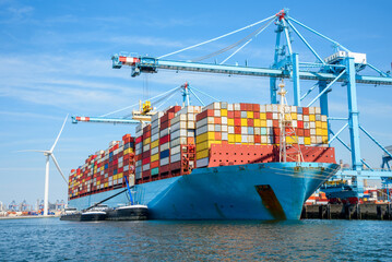 Large cargo ship full loaded with containers moored to a container terminal on a sunny summer day - obrazy, fototapety, plakaty