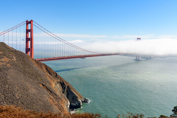 View of Golden Gate bridge partially covered with fog drifting from the ocean on a fall morning