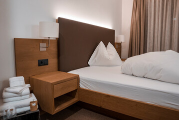 Wooden night table and lamp by white duvet and pillow on bed in illuminated empty room of luxury...