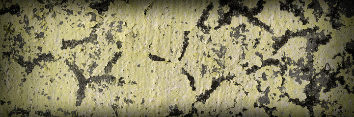 Vintage wall texture. Weathered rough surface of a concrete wall with peeling yellow paint. Wide panoramic texture for background and design.